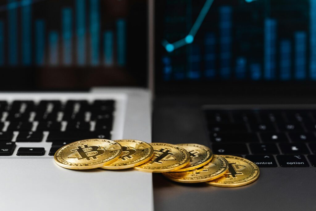 Gold bitcoins placed on laptop keyboards with digital financial graphs in the background.